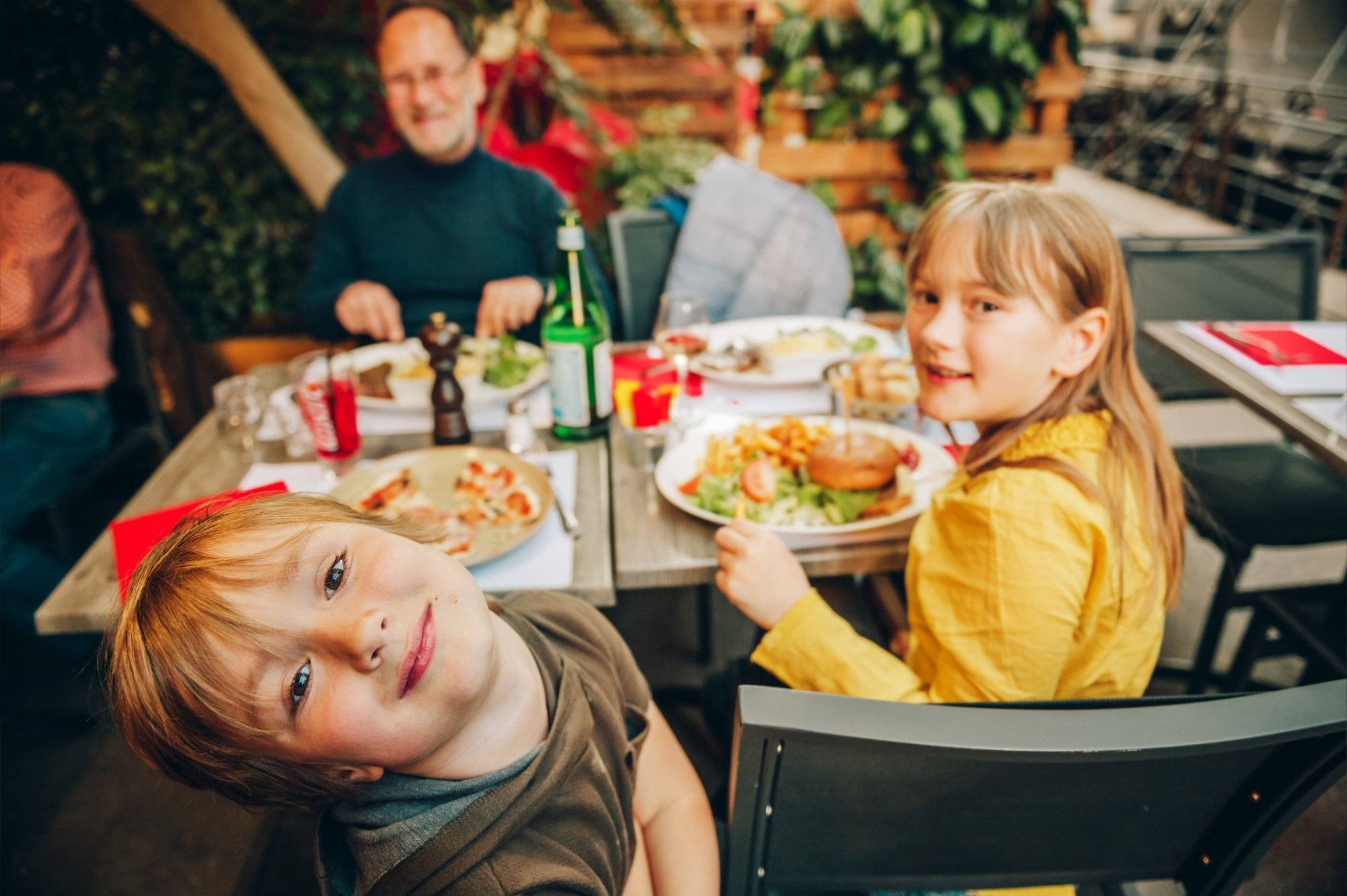 Happy family eating hamburger with french fries and pizza in outdoor restaurant