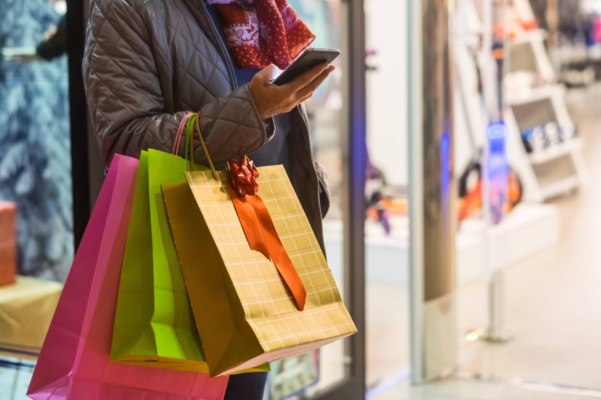 One people alone. A senior woman enjoys evening shopping while taking advantage of offers and discounts. On his arm a lot of shopping bags while she looks at her cell phone